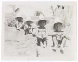 Item 0012. Four young boys wearing only conical straw hats seated on stone steps.