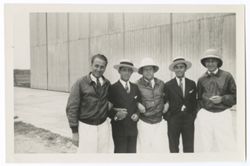 Item 0356. From left, Alexandrov, unidentified man, Eisenstein, Liceaga, Tissé, standing with arms linked outside a large corrugated metal building. (Possibly an airport?)