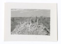 Item 1061. Long shot of a group of people near the top of a hill, with ruins on the opposite side of the summit. This may be the High Priest's Grave.
