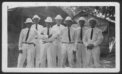 Seven men wearing white uniforms posing outside.
