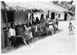 People seated in shade under thatched roof