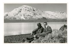Two men sitting in front of a mountain landscape