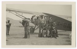Item 0508. Group of men sitting and standing beside a single-engine plane. Eisenstein, seated, second from right - rest unidentified.