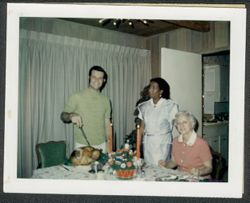 Randy Carmichael carving a turkey with Georgia (Carmichael) Maxwell seated at the table and an unidentified woman in the background.