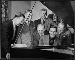 Hoagy Carmichael at piano with five men, including Fenwick Reed, 'Dixie' Heighway, and Branch McCracken, looking on.