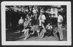 Six unidentified musicians posing while sitting on a car with two unidentified men looking on.