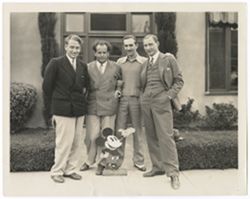 Item 0308. Left to right, Alexandrov, Eisenstein, Walt Disney, Tissé. In front, Mickey Mouse. Standing in front of building entrance, probably at Disney Studios.