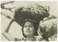 Item 0031. Young Indigenous woman in Items 29-30 above with one decorated basket on her head and one held in her hand. Fruit in both baskets. Head and shoulders.