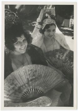Item 0070. Two young women, seated, wearing mantillas and holding fan. The woman at left wears a dark mantilla, the one at right a white one. 