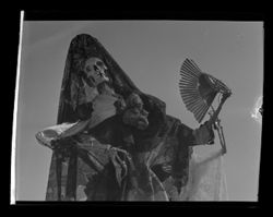 Item 0243. Skeleton wearing dress and mantilla, and holding an open fan.