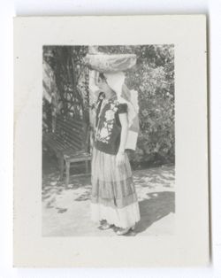 Item 0597. Same young woman seen in Item 27 above, wearing a "weepeel" headdress and holding a large, round, decorated bowl on her head.