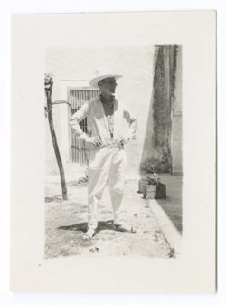 Item 1207. - 1207a. Two similar shots of Tissé in white Stetson, jacket and slacks, in front of an adobe wall with a grilled doorway.