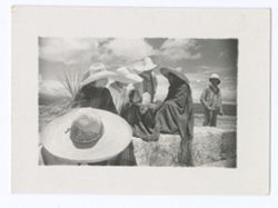 Item 1144. Group of six men to sombreros and ponchos seated on a low wall. Unidentified man (possibly Kimbrough) wearing pith helmet standing behind wall at far right.