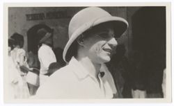 Item 0524. Close-up, right profile, of Tissé, wearing pith helmet, in front of building. A number of people in background. There are two marks or scars on his cheek just at the side of his mouth.
