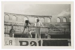 Item 0351. Eisenstein leaning on rail at upper level of bullring stands. Camera on tripod to his right, unidentified man in straw hat in background, left. See Item 338b no. 3 above.
