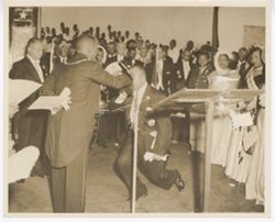 Dignitary bows and kisses a book being held during a formal event as crowd overlooks