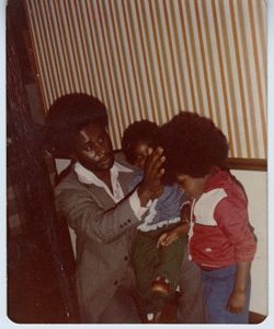 Man in leisure suit fixes boy's hair while balancing another on his knee