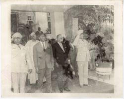 President William V. S. Tubman and guest stand between two saluting military officials at an entrance