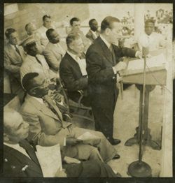 Dignitary speaks from behind a lectern, President Tubman is seated beside him