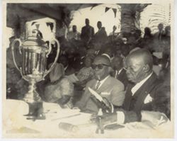 President William V. S. Tubman sits at table in front of crowd with trophy