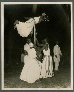 Men hold large pole as man balances on top