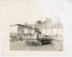 Person stands and waves from car as it passes by a crowd in the street