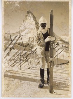 Coocoo in winter dress poses with skiis in front of mountain