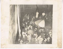 Large group mingle outside with large umbrella in middle