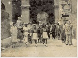 President Tubman and group of men, women and children walk together outside with large columns in background