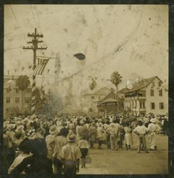 Crowd gathers in the street, looking down the road away from the camera