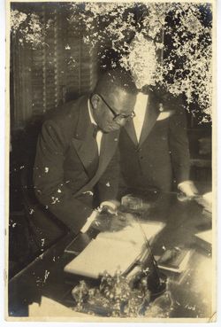 President William V. S. Tubman signs a book as man overlooks