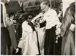 Man in ceremonial dress helps Mrs. Tubman from vehicle