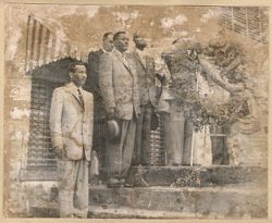 Men in suits stand next to funeral wreath