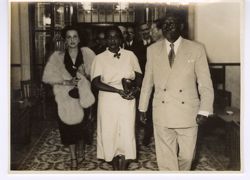 President Tubman and his wife walk with dignitaries down a hall