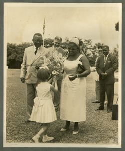 Young girl hands Mrs. Tubman a bouquet of flowers as President William V. S. Tubman and others stand by