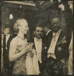 Two men in decorated military uniform stand with woman in ballgown
