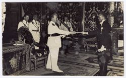 Two men in decorated formal dress pass ceremonial object to each other