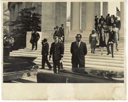 Men and women walk down stairs toward vehicles while flag flys in background