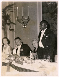 Man stands at table while others look on
