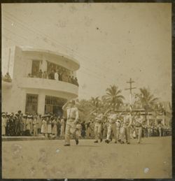 Military men march in parade and salute with crowds watching in front of Executive Pavilion