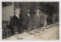 President Tubman stands behind a dining table with other dignitaries