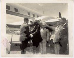Military officials and officials greet a man as he gets off an airplane on runway