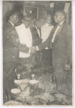 Men shake hands while President William V. S. Tubman looks on