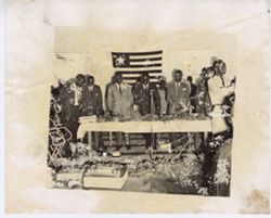 President William V. S. Tubman and others sit behind table in front on flag