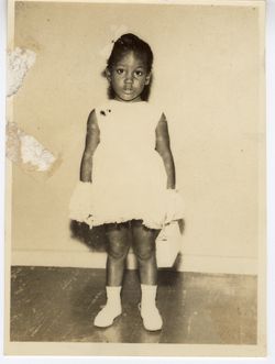 Small girl wearing a white dress, shoes, gloves and matching purse poses