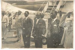 Large group of men in business suits and military dress pose for portrait in front of airplan