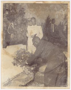 President William V. S. Tubman places flowers on a monument, observed by military officers