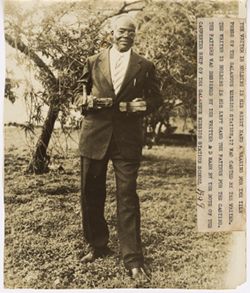 Man standing outside with the following written: The writer is holding in his right hand a bearing for the tile press of the Galangue Mission Station. It was casted by the writer. The writer is holding in his left hand the pattern for the casting. The pattern was designed by the writer and made by the boys of the carpenter shop of the Galangue Mission Station School 1949
