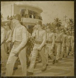 Military men march in parade past crowds in front of Executive Pavilion