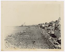 A crane lifts stones in the distance next to a body of water